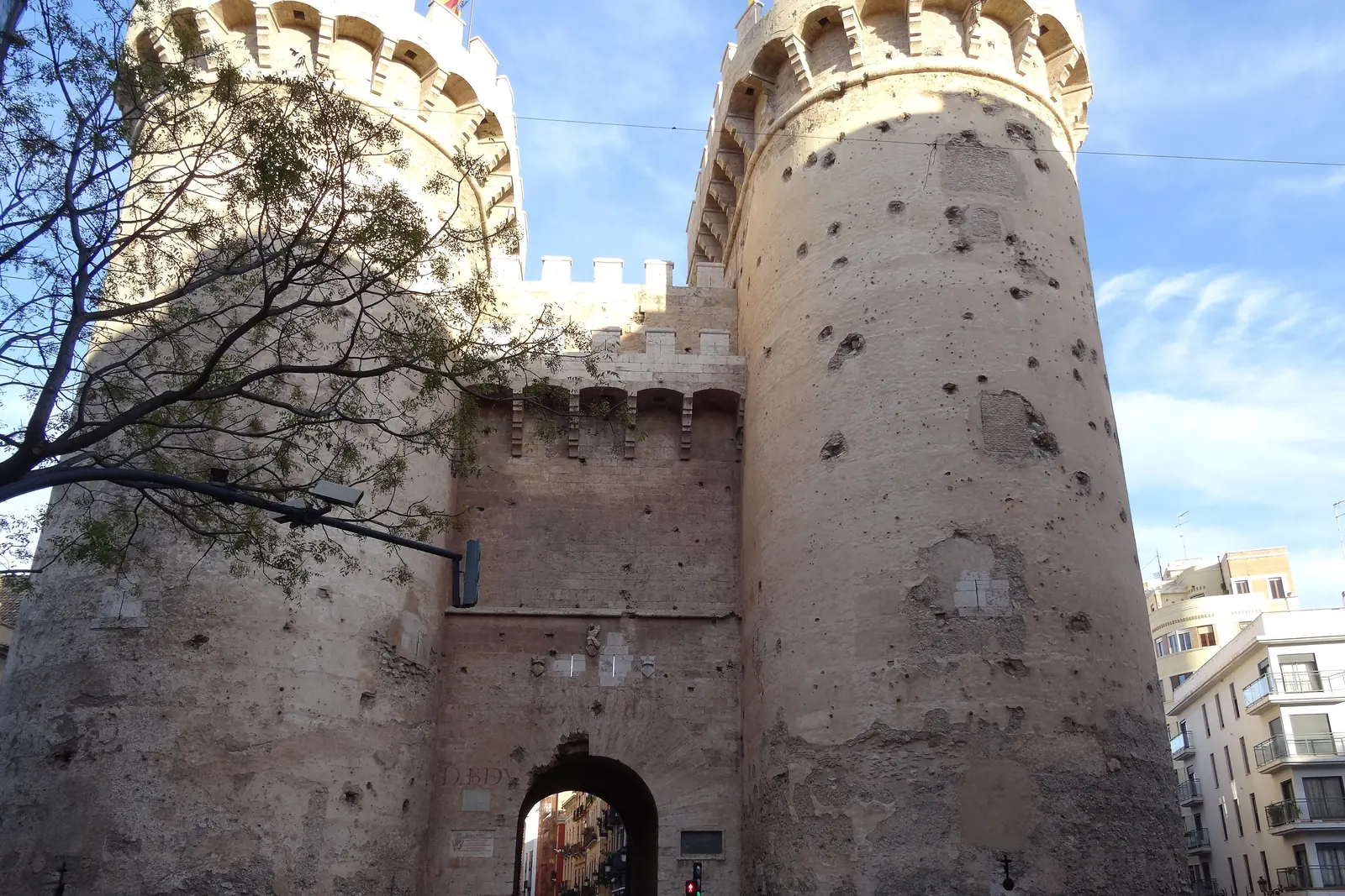 The two round towers of the Torres de Quart in Valencia, their stone pitted with old cannonball and bullet marks, with the gateway arch between them